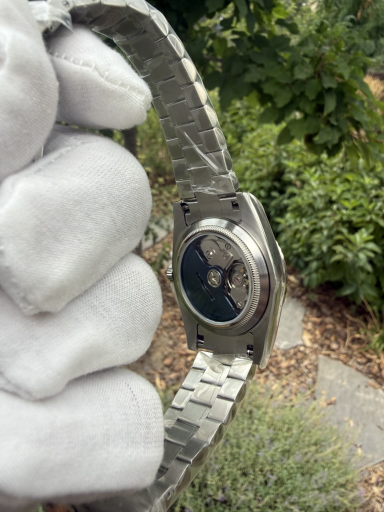 Blue Sunburst Dial Homage — caseback detail, held in a gloved hand outdoors