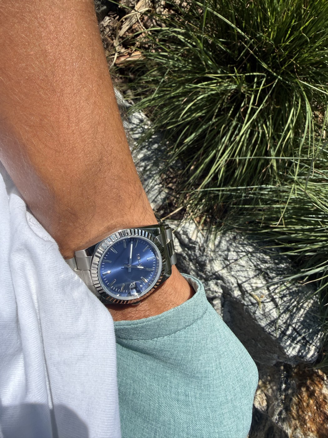 A blue sunburst dial watch worn on the wrist, resting against granite and mountain grass